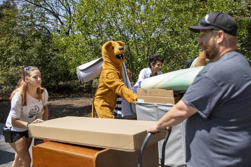 A parent, student, Chancellor Pyati and the Nittany Lion mascot move items into the residence halls